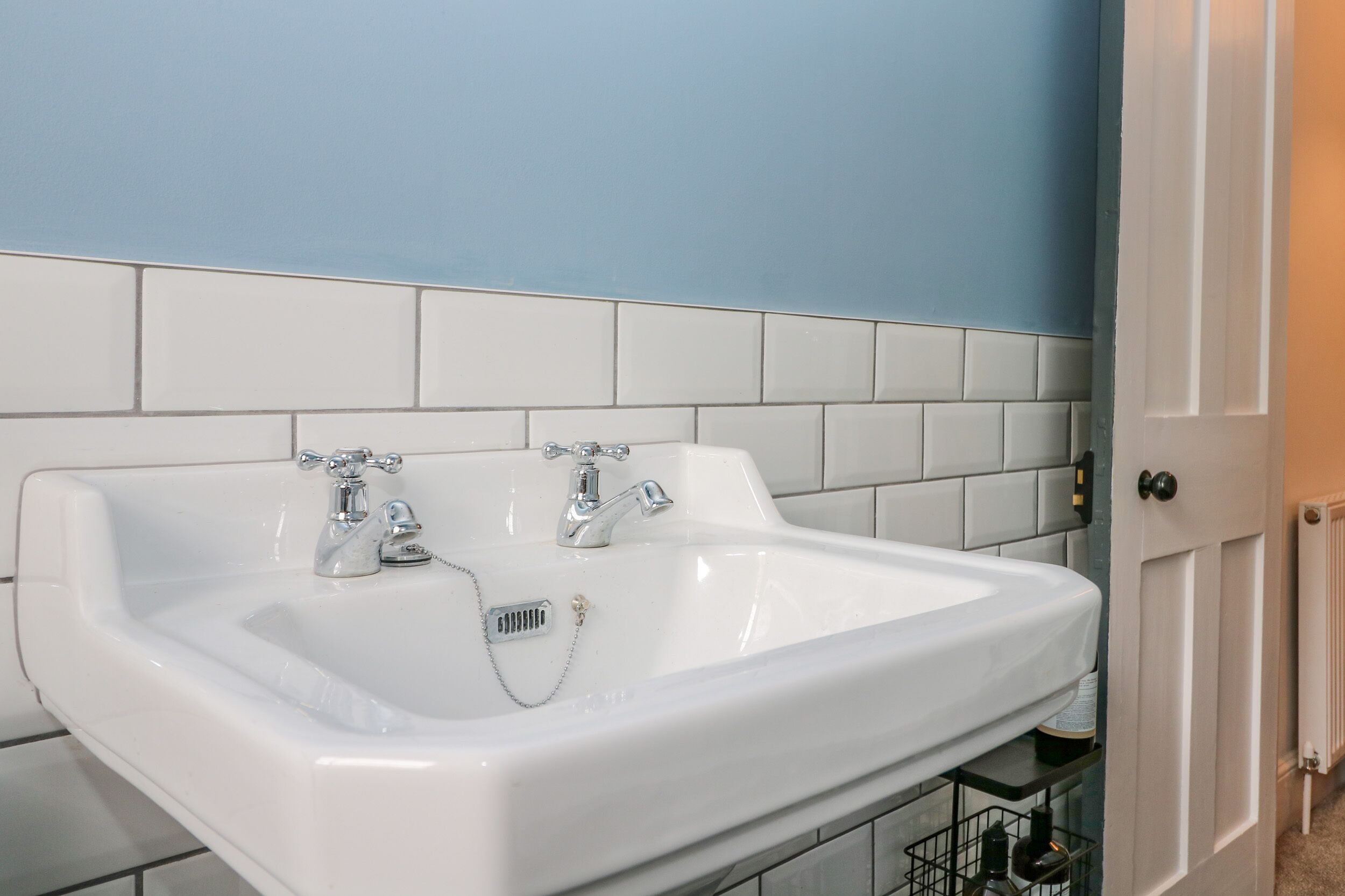 A white bathroom sink with two faucets, a towel rack below, and a white door to the right.