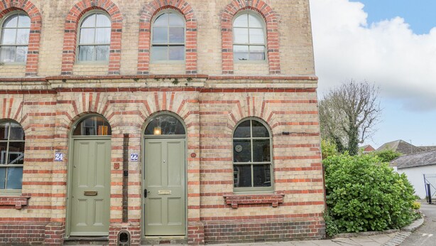 Un edificio histórico con tres ventanas de arco y dos puertas verdes, números 24 y 22.