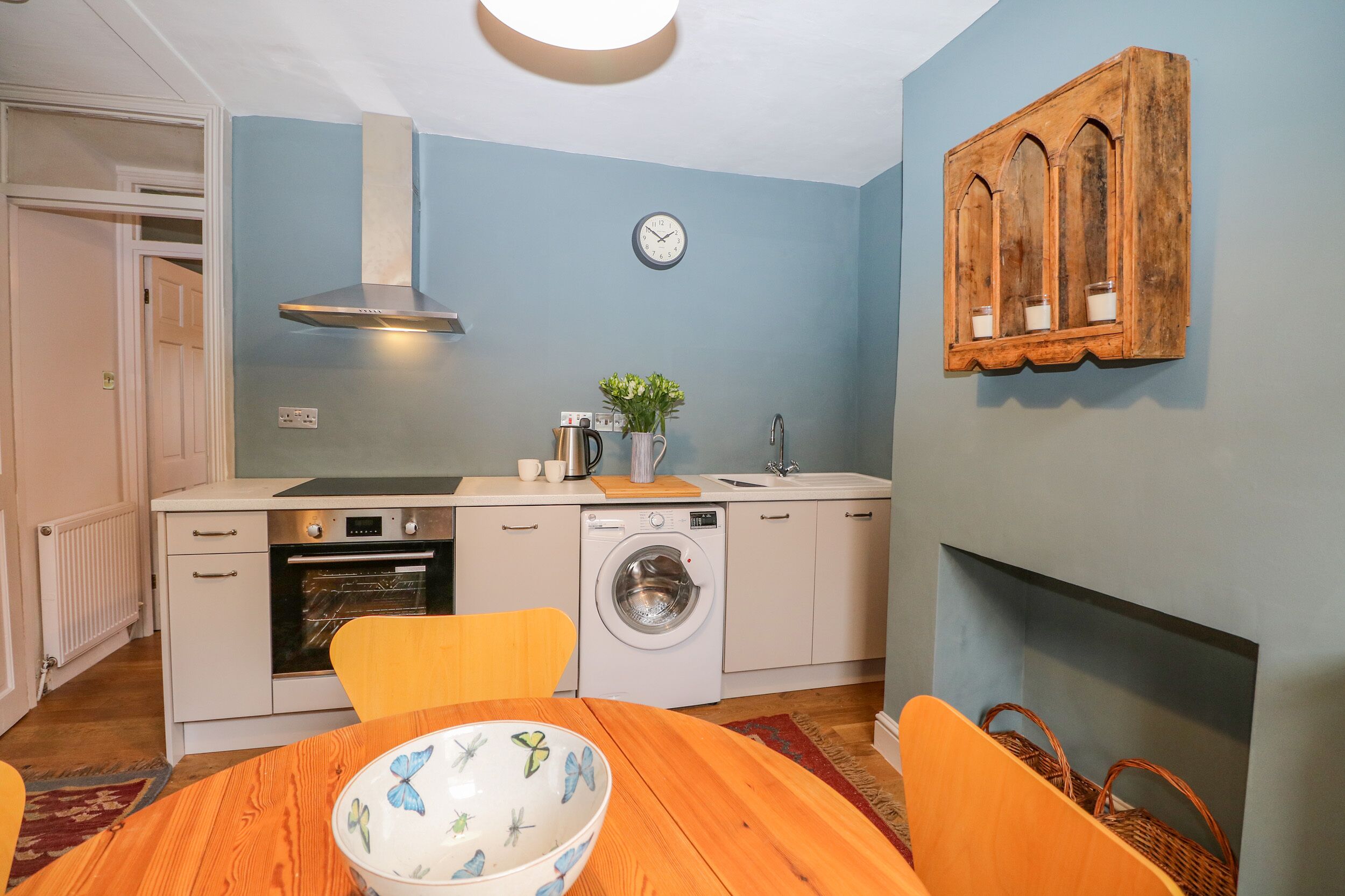 Een kleine keuken met een wasmachine, oven en een klok aan de muur.