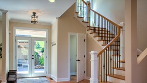 A spacious foyer with a wooden staircase, a glass door leading outside, and a light-colored carpet.