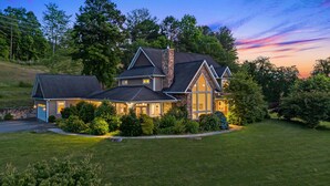 A large, two-story house with a stone chimney, multiple windows, and a well-maintained lawn.