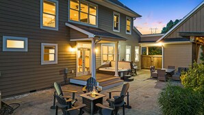 A two-story house with a covered patio area featuring outdoor seating and a hot tub.