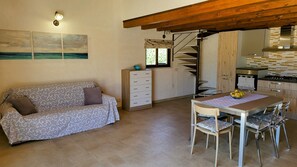 A cozy living area with a sofa, a wooden cabinet, a dining table with chairs, and a kitchen area with a stove and cabinets.