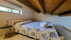 A bedroom with a bed, a nightstand, a lamp, and a window.