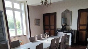 A dining area with a long table set for six, a chandelier, and a view of the outdoors through a window.