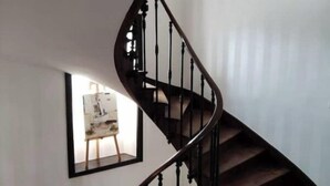 A spiral staircase with wooden steps and black balusters, leading to a landing area with a framed artwork.
