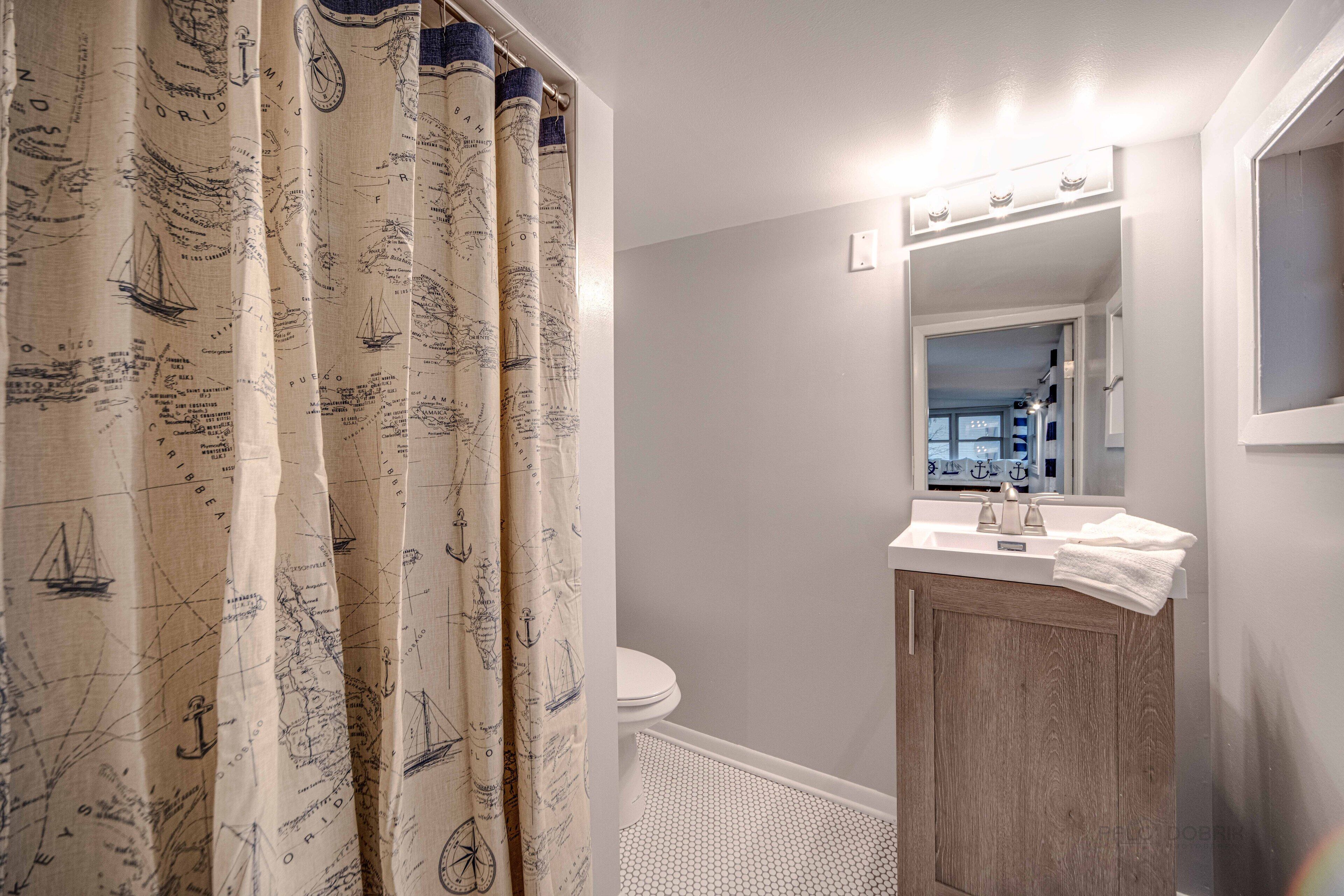 A bathroom with a nautical-themed shower curtain, a white toilet, and a wooden vanity with a mirror above the sink.