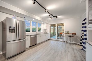 A modern kitchen with a stainless steel refrigerator, white cabinets, and a large window.