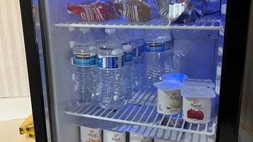 Un refrigerador con estantes llenos de agua embotellada, yogur y aperitivos envasados.