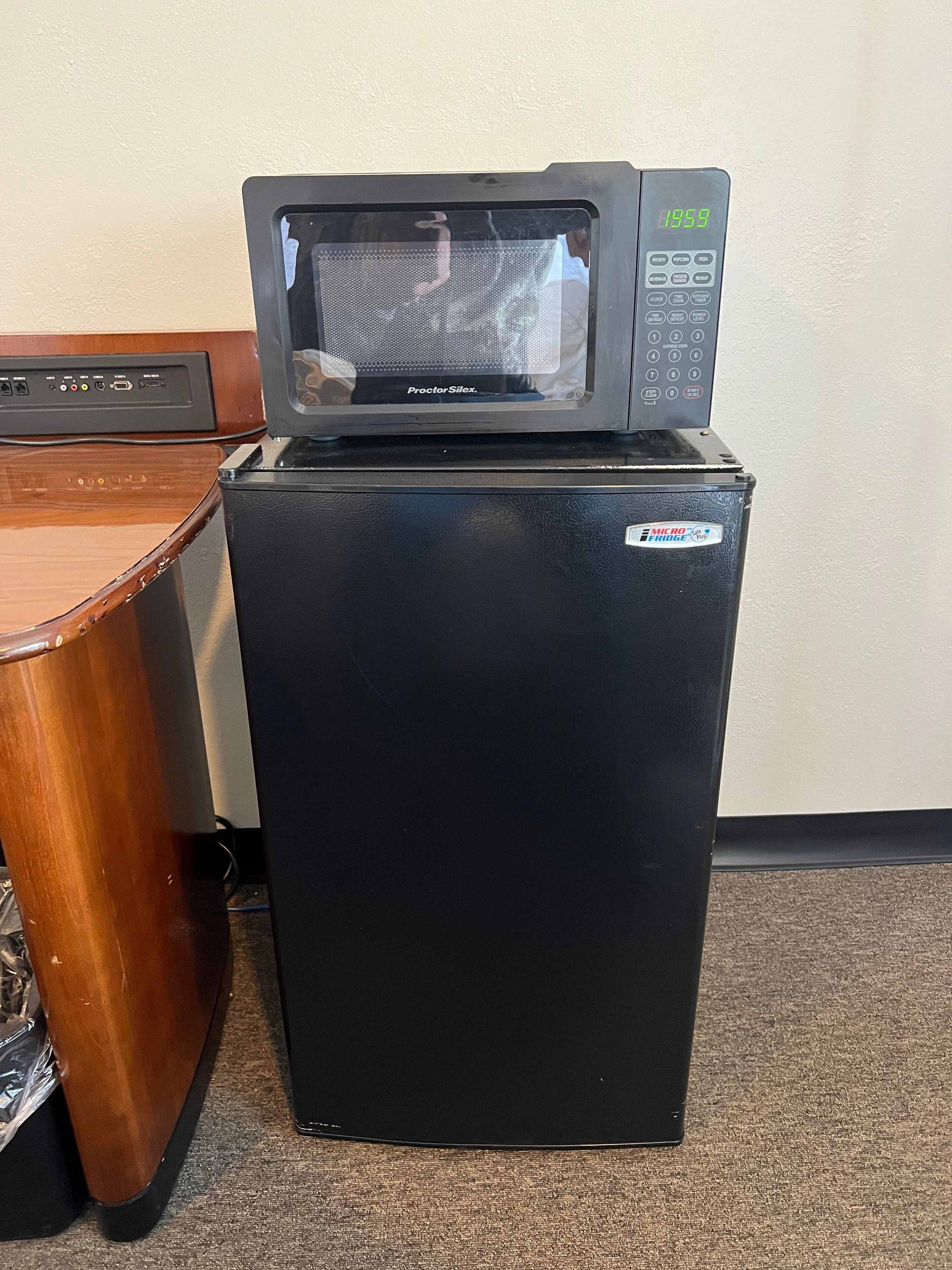 Un refrigerador pequeño negro con un microondas encima, un gabinete de madera y piso alfombrado.