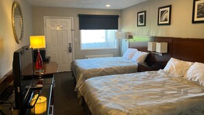 Habitación de hotel con dos camas, un escritorio con lámpara, un espejo y cuadros en la pared.