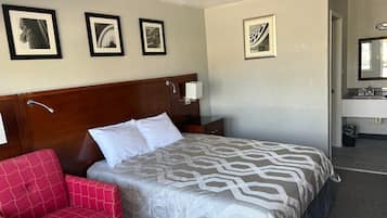 Quarto de hotel com cama, mesa de cabeceira, abajur, cadeira e quadros na parede.