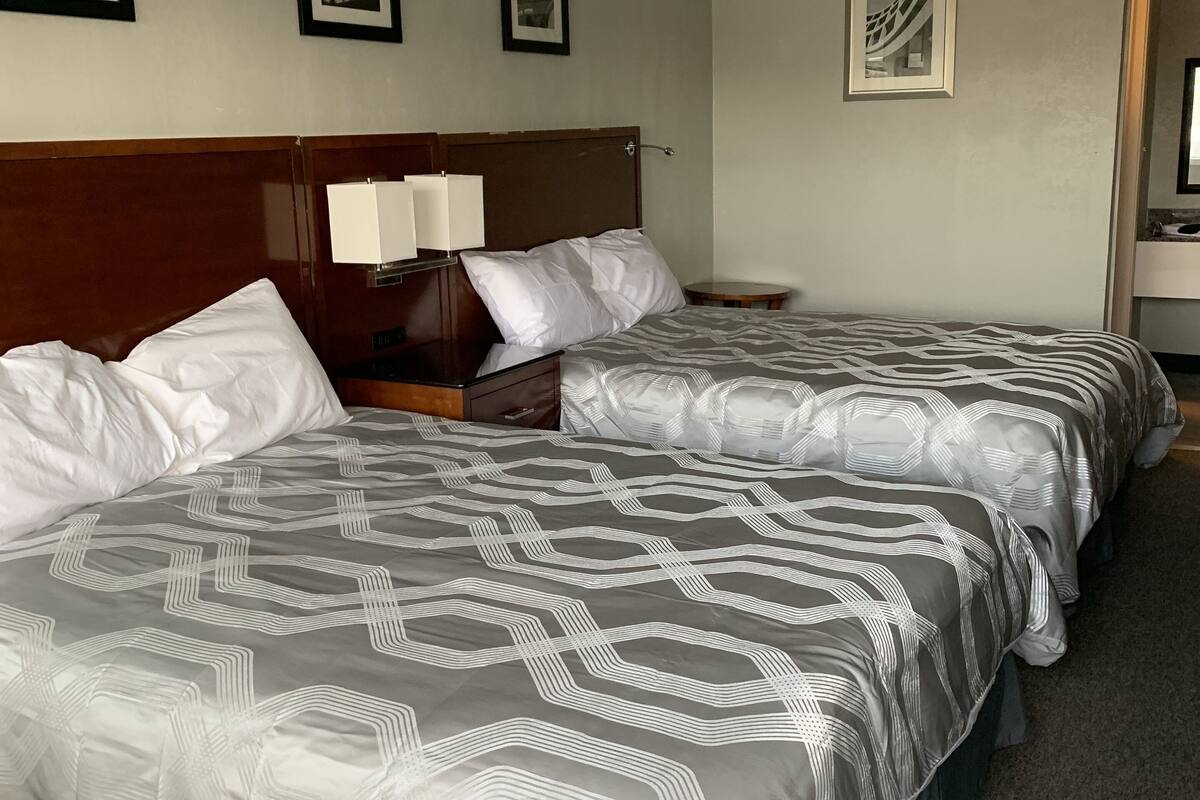 Une chambre d’hôtel avec deux lits, une tête de lit en bois, une table de chevet avec une lampe et des tableaux encadrés au mur.