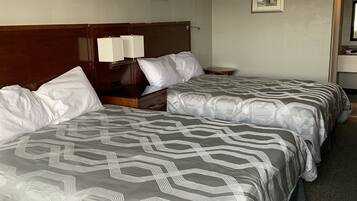 A hotel room with two beds, a wooden headboard, a nightstand with a lamp, and framed pictures on the wall.