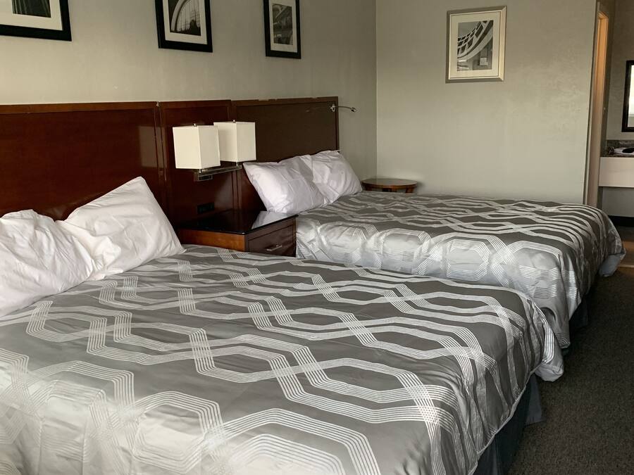 A hotel room with two beds, a wooden headboard, a nightstand with a lamp, and framed pictures on the wall.