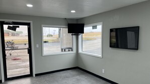 Una habitación con dos ventanas, un televisor de pantalla plana montado en la pared y una puerta con un tapete de bienvenida.