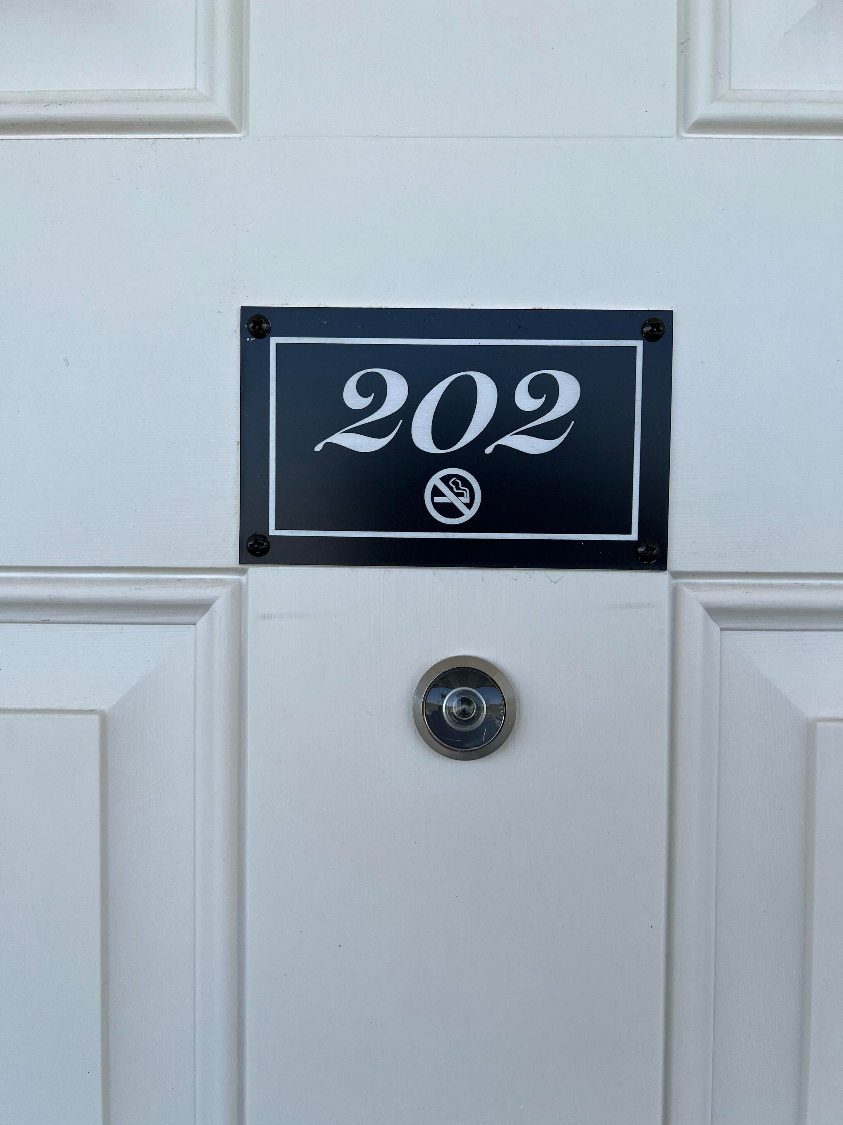 Una puerta con un cartel negro que muestra el número 202 y un símbolo de prohibido fumar.