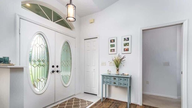 A hallway with a wooden floor, a white door with a glass panel, a blue console table, and a small rug.