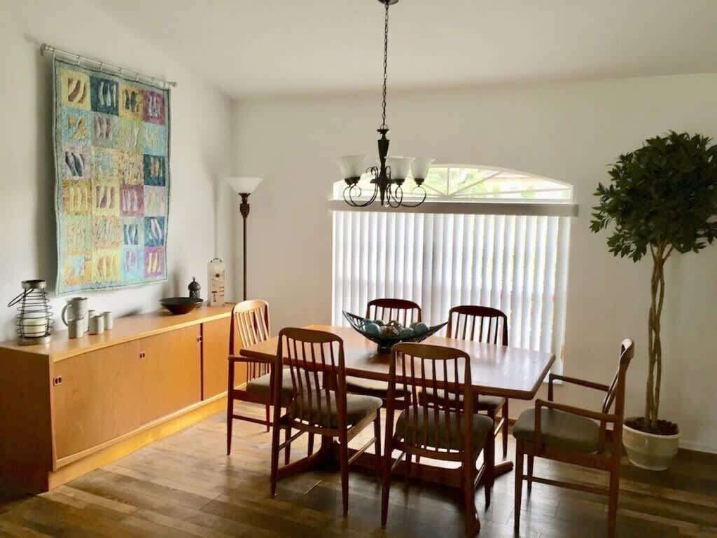 A dining area with a wooden table and chairs, a chandelier, a potted plant, and a window with blinds.