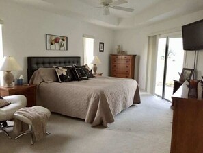 Une chambre à coucher avec un grand lit, une commode, un téléviseur et un ventilateur de plafond.