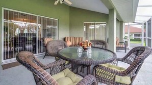 A covered patio area with wicker furniture, a glass table, and a ceiling fan.