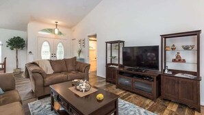 A living room with a brown leather sofa, a wooden coffee table, a flat-screen TV, and a cabinet with decorative items.