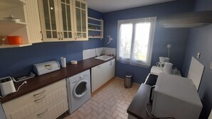 A compact kitchen with white cabinetry, a washing machine, a sink, and a window providing natural light. - Quiet gite with garden 300 m from Le Guichet rer station (Orsay)