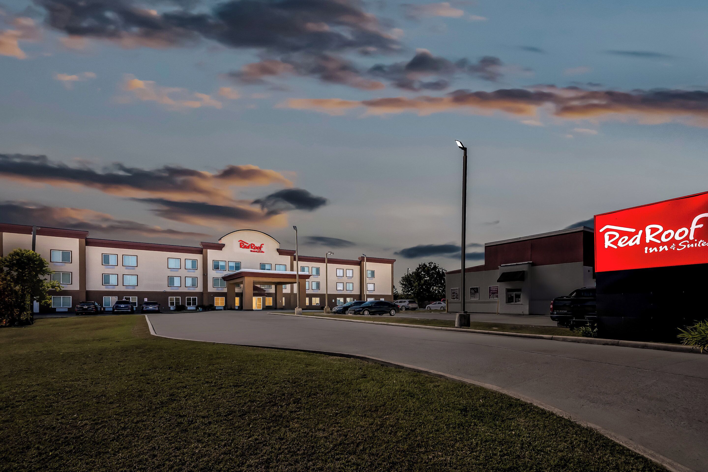 A Red Roof Inn & Suites building with a parking lot, a grassy area, and a clear sky with clouds.