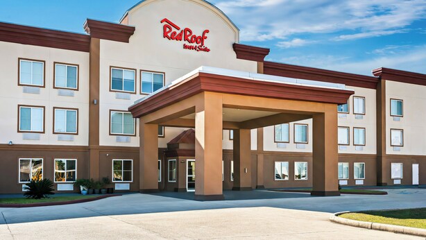 Edificio de Red Roof Inn & Suites con entrada cubierta, múltiples ventanas y cielo despejado.