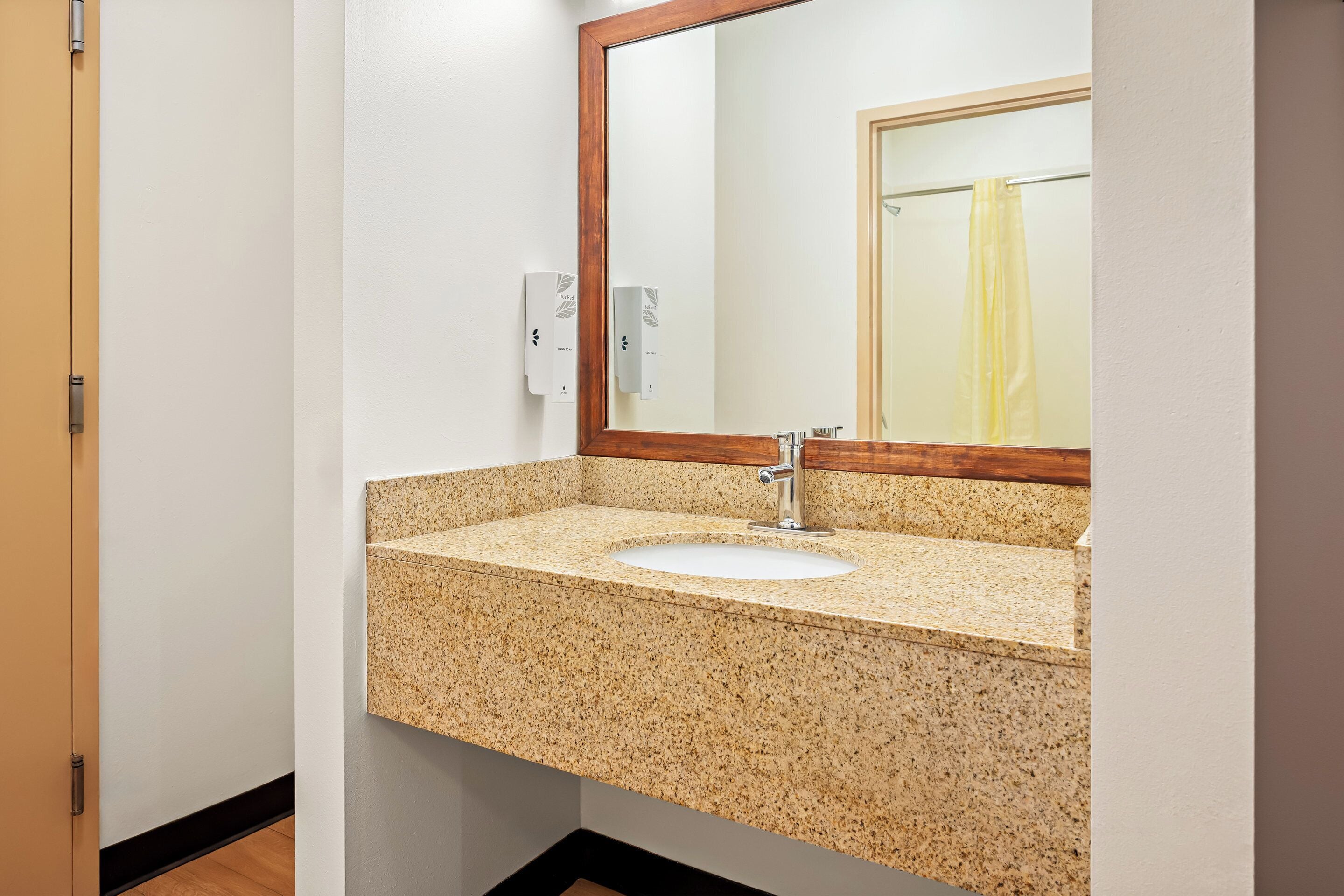 Une salle de bain avec un lavabo doté d’un plan de travail en granit, un miroir encadré en bois et un porte-serviettes avec une serviette jaune.