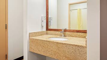 Une salle de bain avec un lavabo doté d’un plan de travail en granit, un miroir encadré en bois et un porte-serviettes avec une serviette jaune.