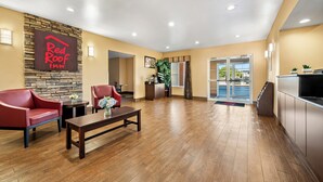 A Red Roof Inn lobby with a stone accent wall, wooden flooring, red leather chairs, a coffee table, and a reception desk. - Red Roof Inn & Suites Houma (Houma)