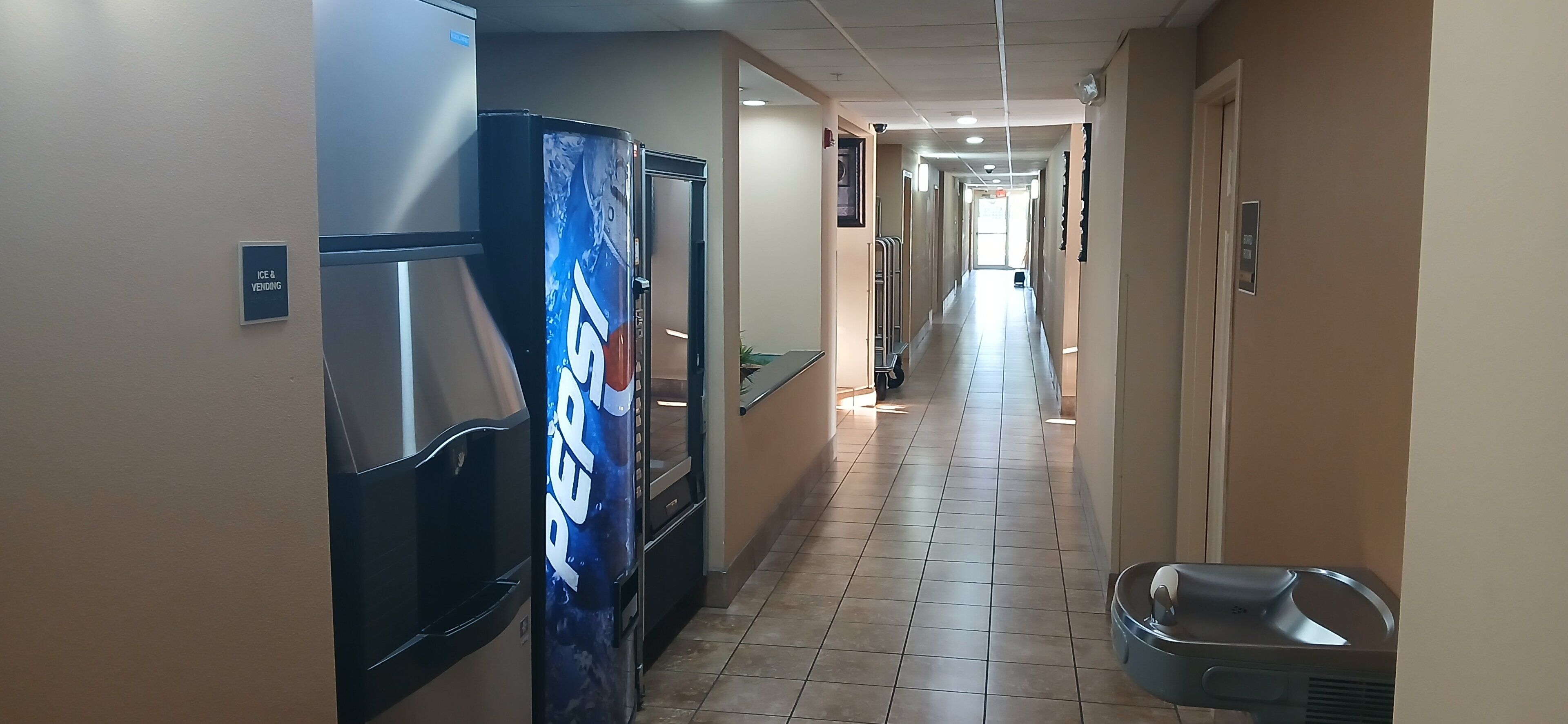 A hotel hallway with vending machines, a trash bin, and a sign for ice and water.