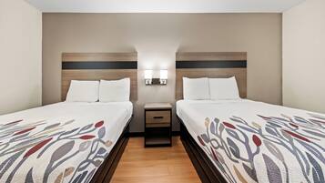 A hotel room with two beds, a nightstand with a lamp, and a wooden floor.