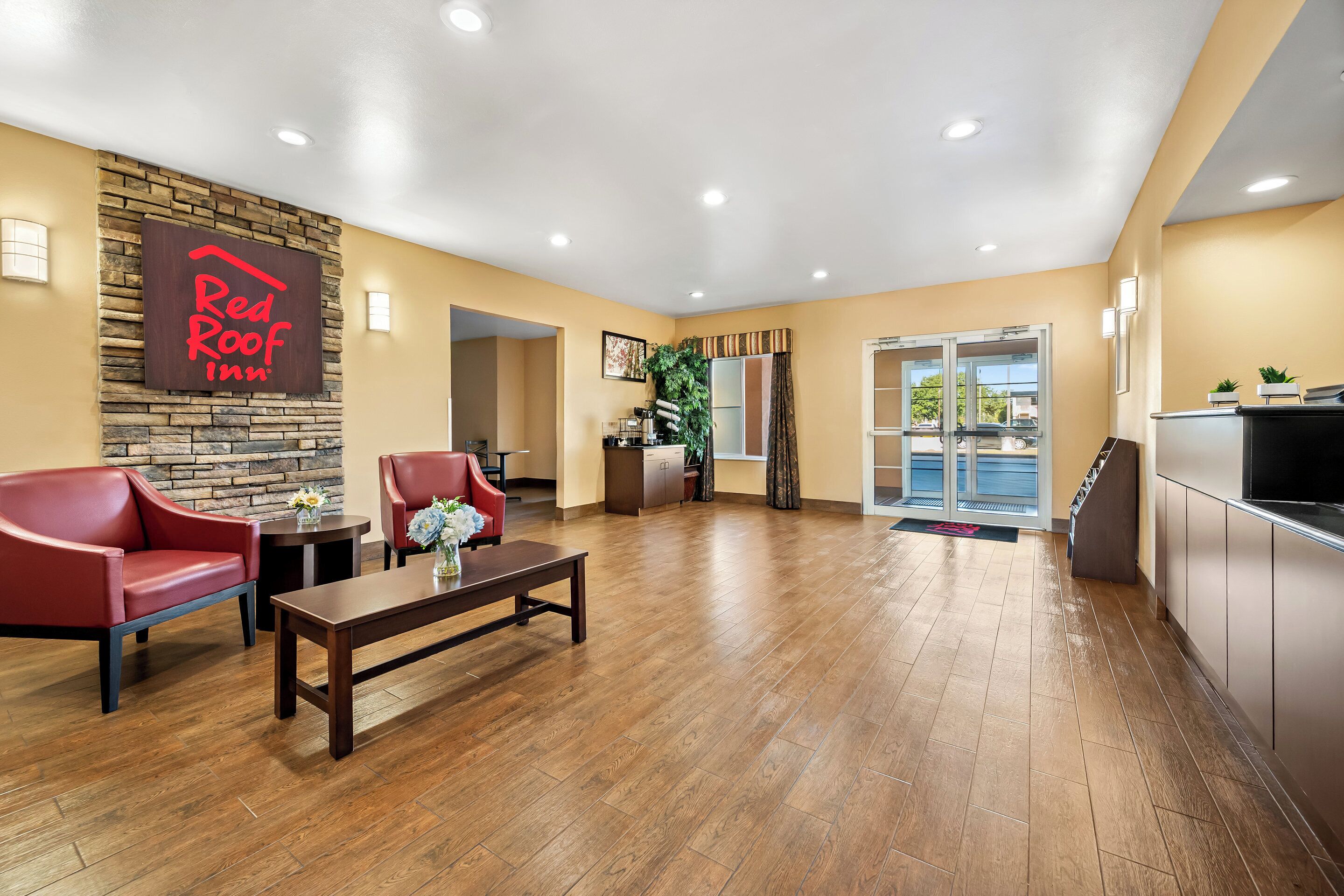 Vestíbulo de Red Roof Inn con una pared decorativa de piedra, suelo de madera, sillas de cuero rojo, una mesa de centro y una recepción.