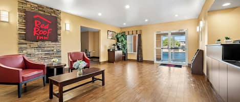 A Red Roof Inn lobby with a stone accent wall, wooden flooring, red leather chairs, a coffee table, and a reception desk.