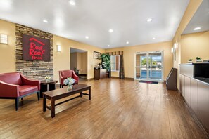 A Red Roof Inn lobby with a stone accent wall, wooden flooring, red leather chairs, a coffee table, and a reception desk.