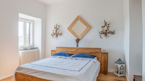 Une chambre à coucher avec un lit en bois, une fenêtre, un radiateur et un miroir fixé au mur.