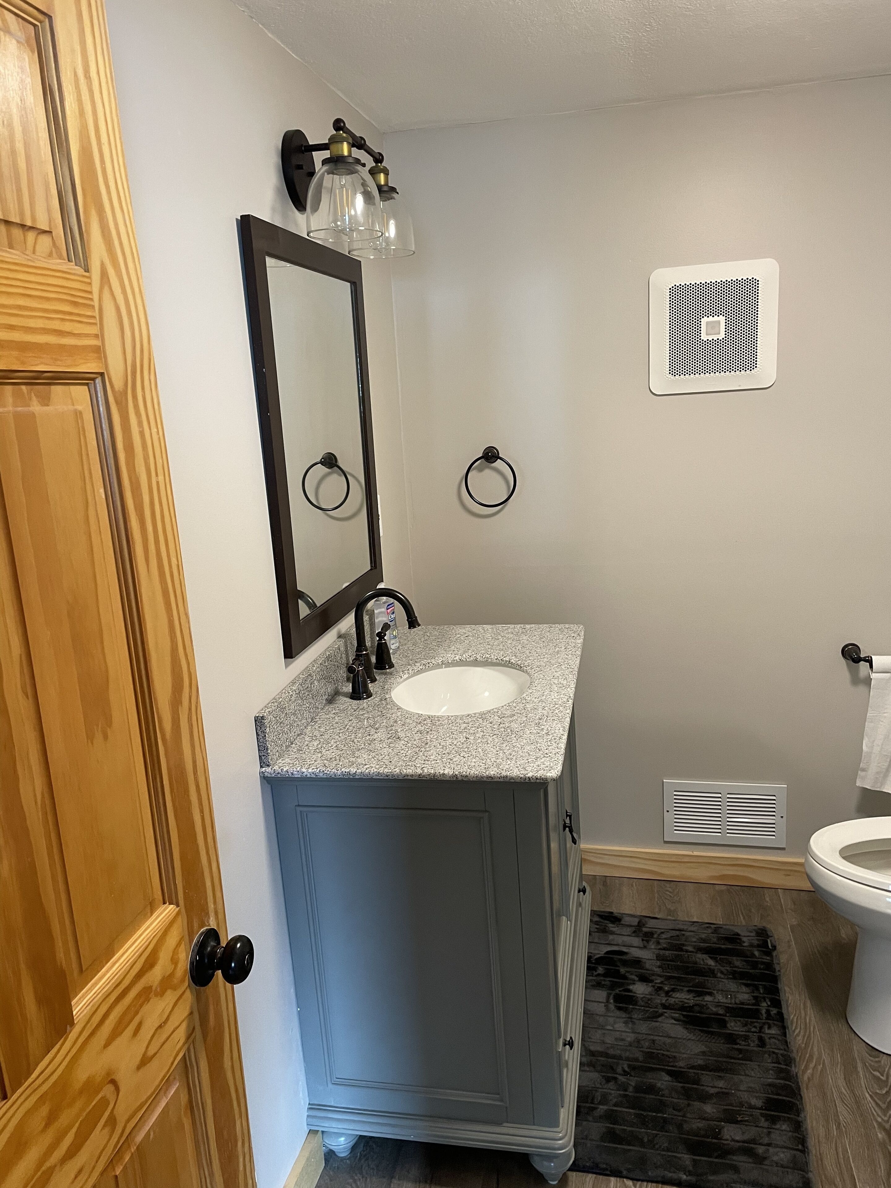A bathroom with a granite countertop sink, a mirror, a towel ring, and a vent.
