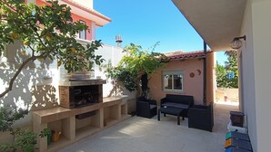 En udendørs terrasse med integreret grill, siddepladser og udsigt til den tilstødende bygning.