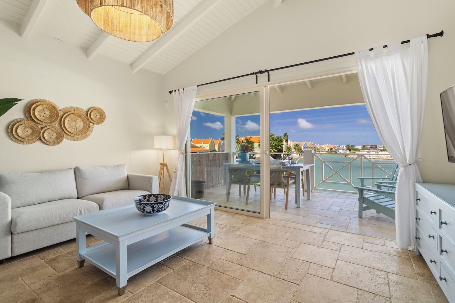 Un balcon avec une table et des chaises, un canapé, un téléviseur et une vue sur la plage.