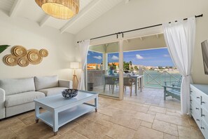 Ein Balkon mit Tisch, Stühlen, einer Couch, einem Fernseher und Blick auf den Strand.