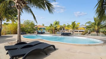 Piscina com espreguiçadeiras, palmeiras e um edifício ao fundo.