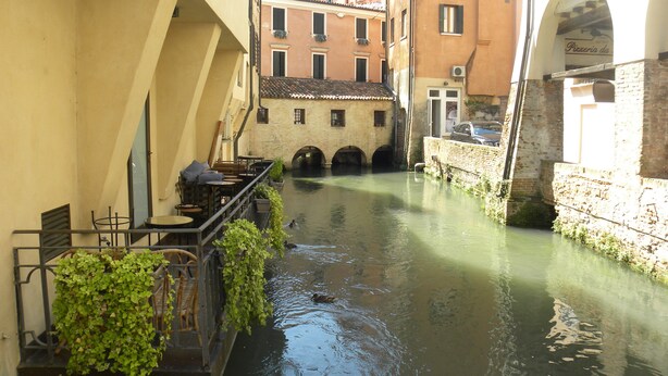 A narrow canal flanked by buildings with outdoor seating and a bridge. - DARK PORCH DELUXE APARTMENT - HISTORIC CENTER (Treviso)