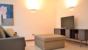 A modern living room with a sofa, ottoman, TV, and bookshelf. - DARK PORCH DELUXE APARTMENT - HISTORIC CENTER (Treviso)