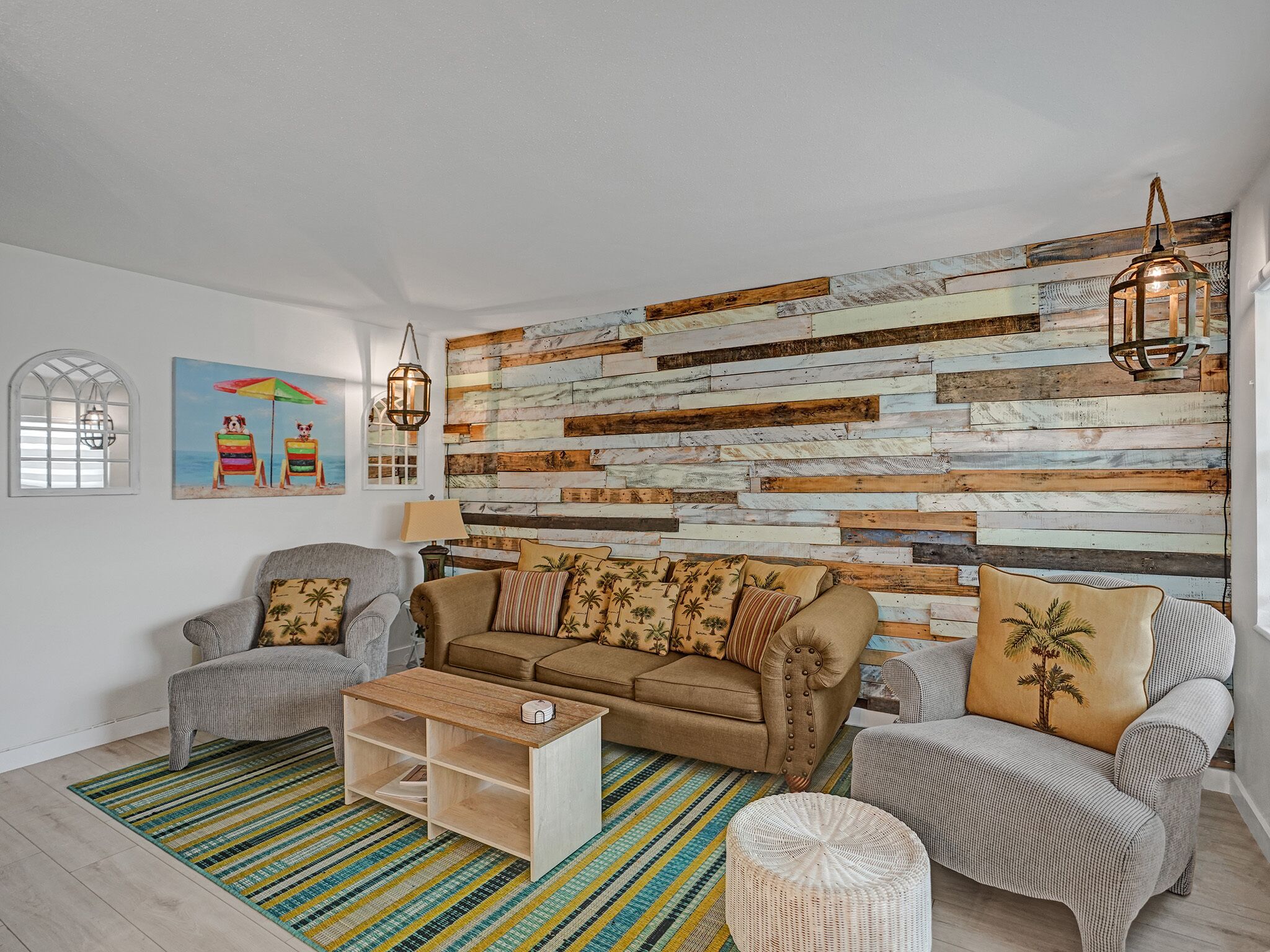 A living room with a wooden plank wall, a brown sofa, two armchairs, a coffee table, and a striped rug.