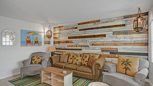A living room with a wooden plank wall, a brown sofa, two armchairs, a coffee table, and a striped rug.