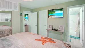 A bedroom with a bed, a TV, and a bathroom with a shower curtain.