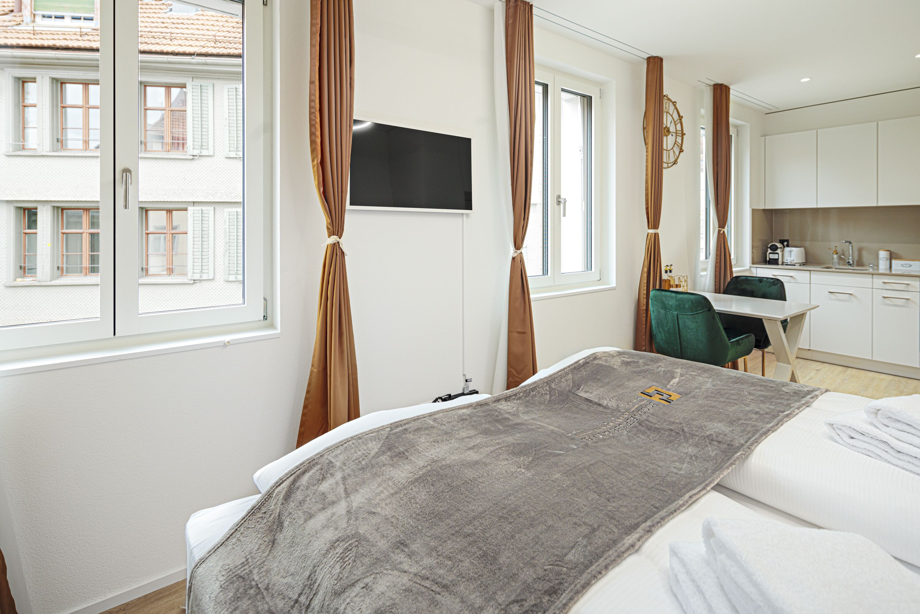 A hotel room with a bed, a desk, a chair, a television, and a view of the outside.