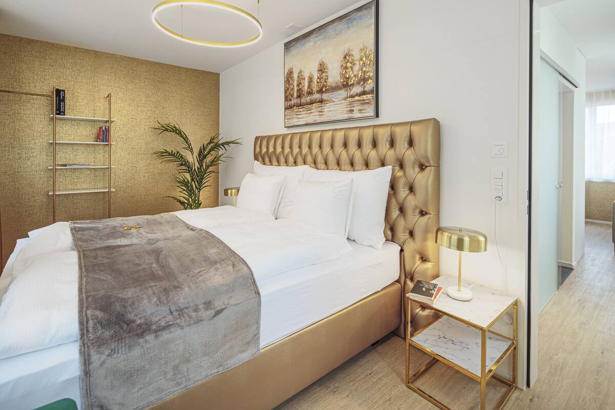 A modern bedroom with a tufted headboard, a bedside table with a lamp, and a painting on the wall.